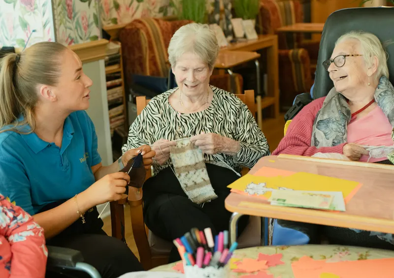 Caregiver assisting older women with knitting