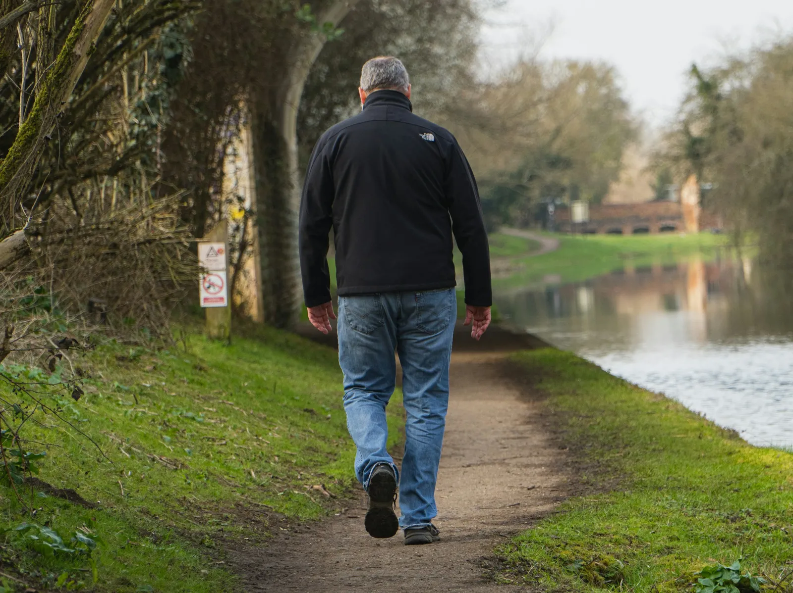 An older adult walking along a peaceful waterside path